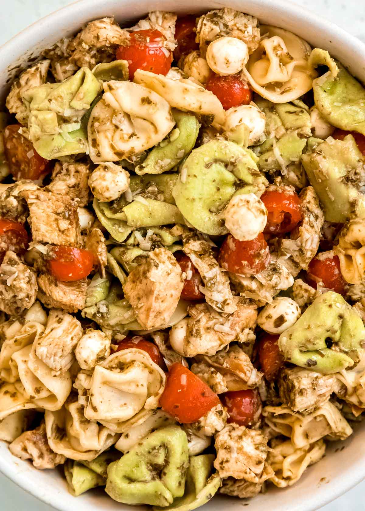 closeup shot of tortellini pasta salad with pesto, mozzarella, and tomatoes.