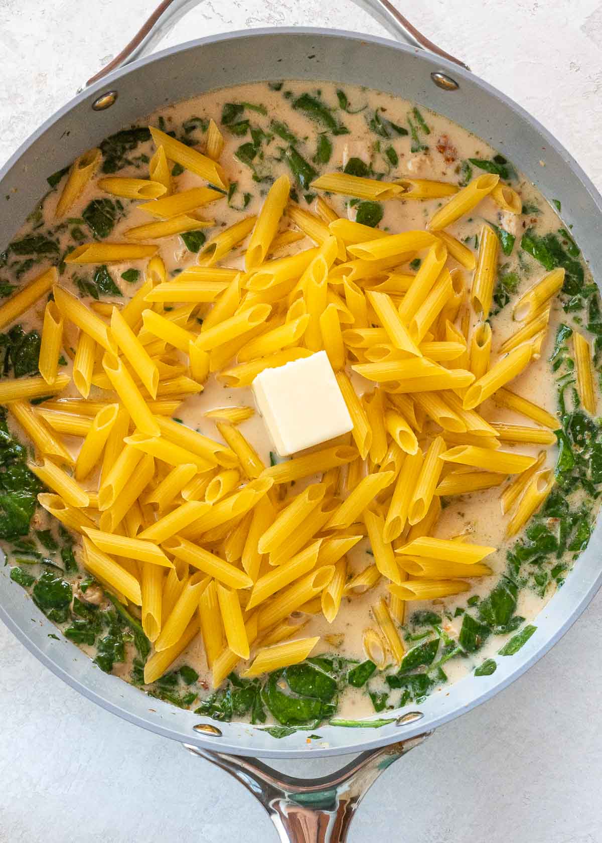 penne being added to skillet with other tuscan chicken pasta ingredients