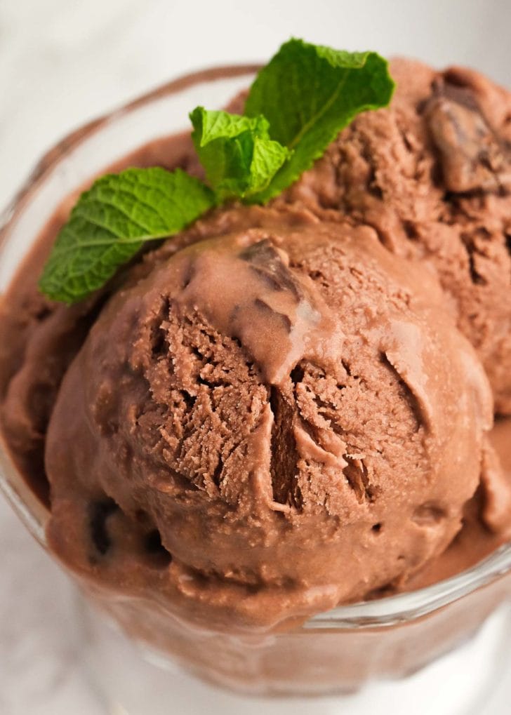 Creamy chocolate mint ice cream with Andes chocolate mints in a glass bowl, topped with a mint leaf garnish