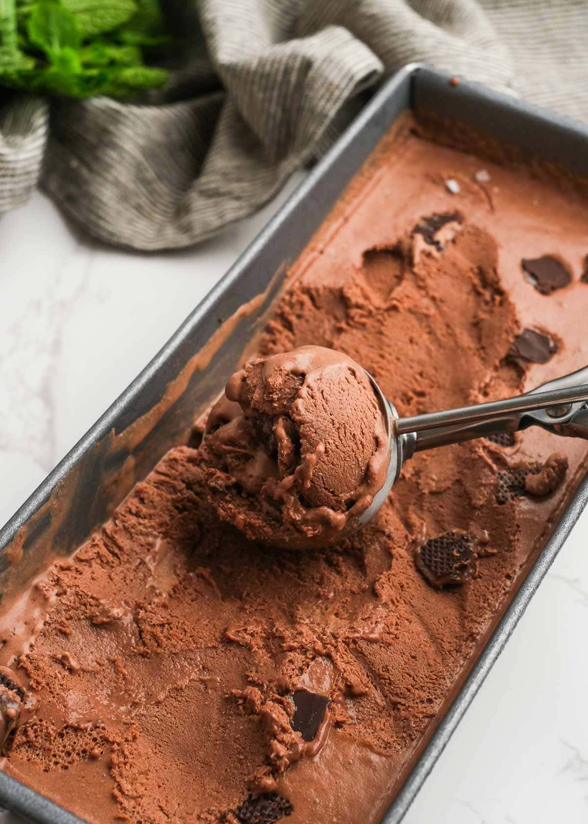 a loaf pan full of chocolate mint ice cream and a scoop full of the homemade chocolate ice cream with andes mints
