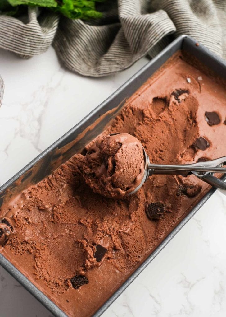 A scoop picking up a big spoonful of chocolate mint ice cream dotted with crushed Andes mints