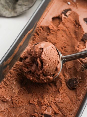 Closeup view of creamy chocolate ice cream dotted with Andes mints; a scoop full lying on a loaf pan full of chocolate mint ice cream
