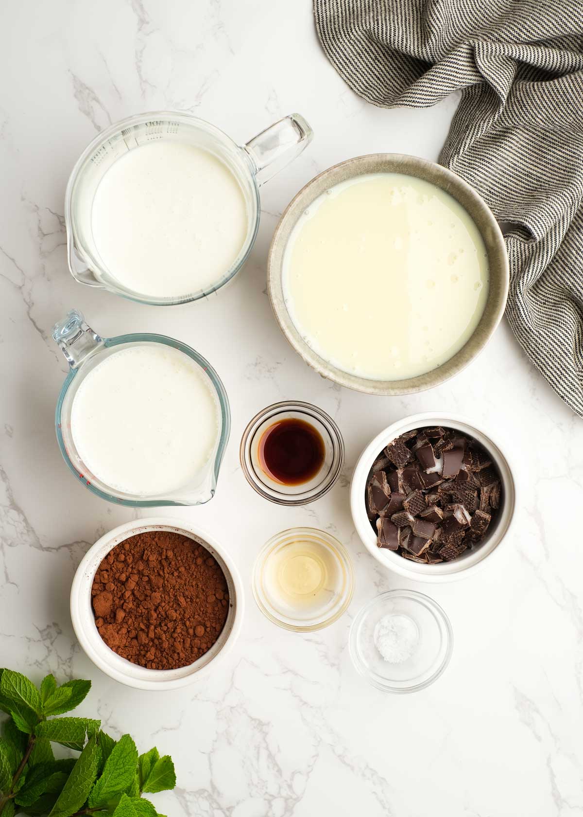ingredients for chocolate mint ice cream in individual bowls on a marble background