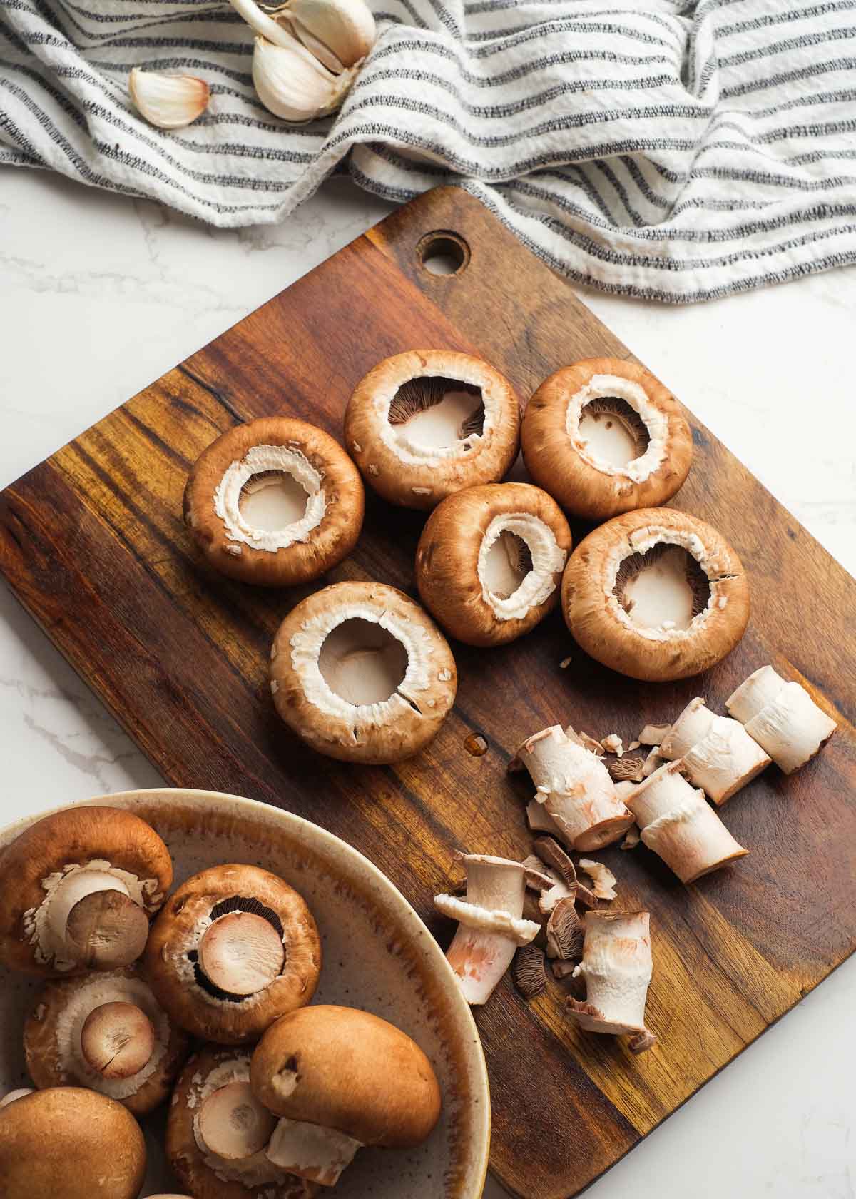 cleaned mushrooms separated from their stems on a wooden cutting board in preparation for stuffed mushrooms recipe