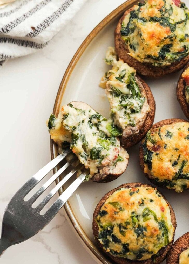 a fork slicing into a cheesy crab stuffed mushrooms with spinach, bacon, and cheese