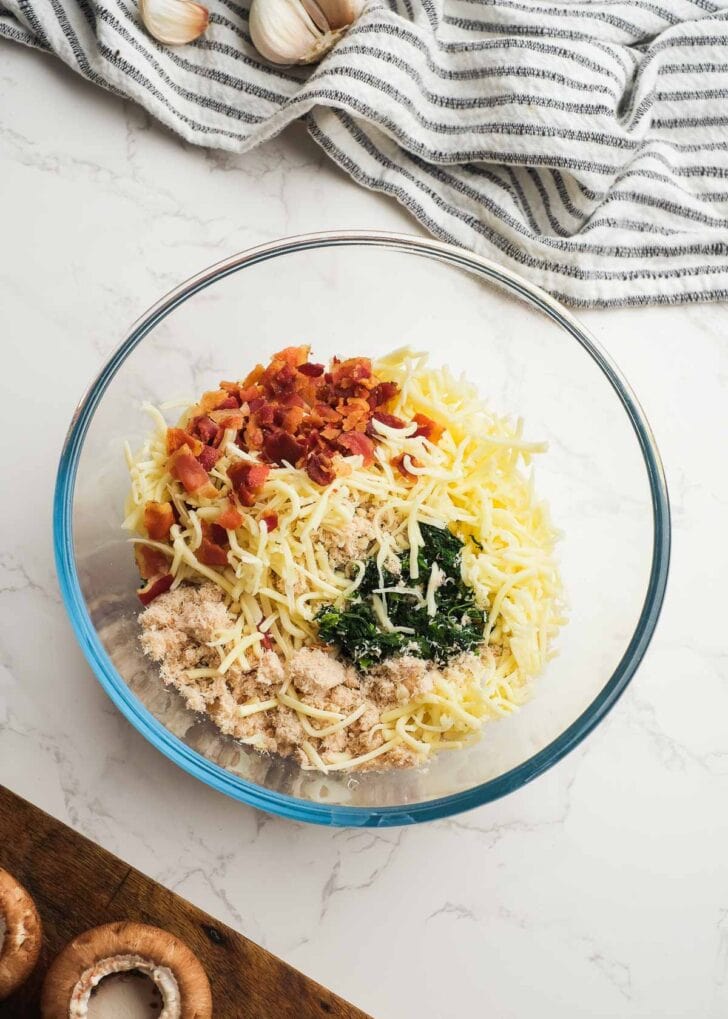 cheese, bacon, cream cheese, sour cream, spinach, and crab meat in a glass bowl