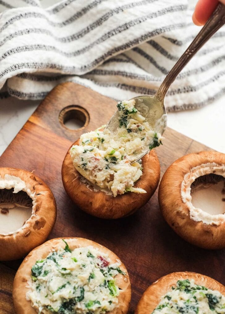 a hand spooning the creamy crab and bacon mixture into small portobello mushrooms