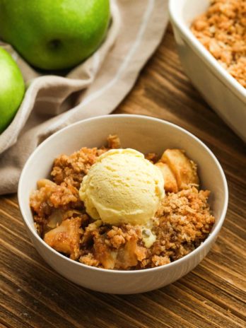overhead image of apple crisp and ice cream in a white bowl on wooden table