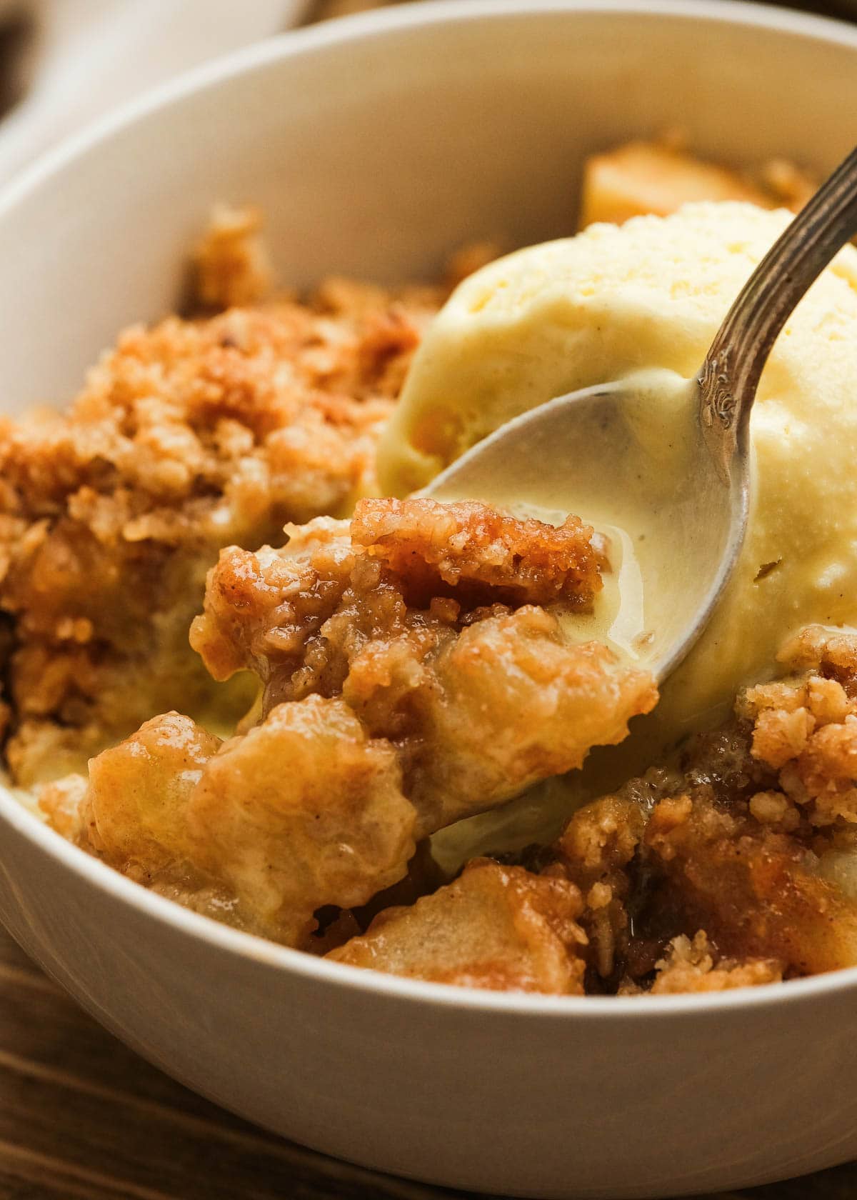 close up image of a spoonful of apple crisp and ice cream in white bowl