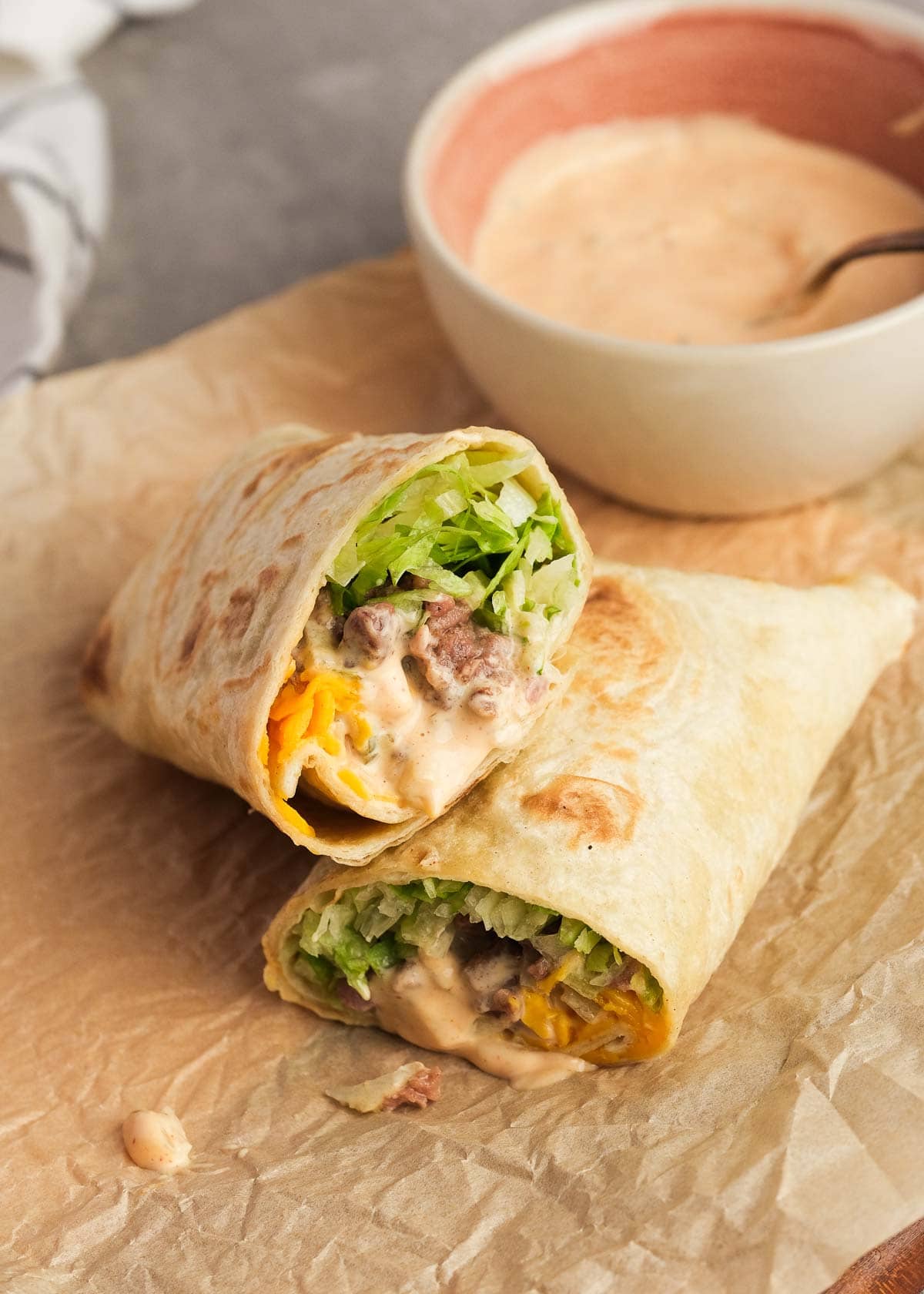 one big mac wrap sliced in half and stacked on parchment paper beside a bowl full of extra big mac sauce