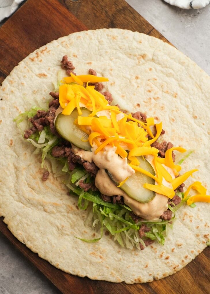 a tortilla topped with shredded lettuce, chopped onions, seasoned beef, big mac sauce, shredded cheese, and sliced pickles