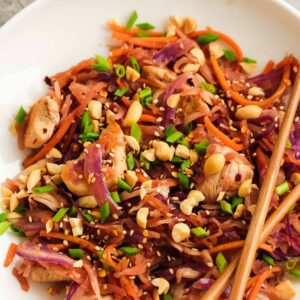 chopsticks crossed over chicken stir fry with purple cabbage, carrots, and a crunchy garnish of green onions and nuts