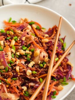 two chopsticks over a white dish loaded with colorful chicken egg roll in a bowl