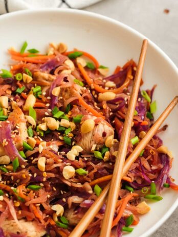 two chopsticks over a white dish loaded with colorful chicken egg roll in a bowl