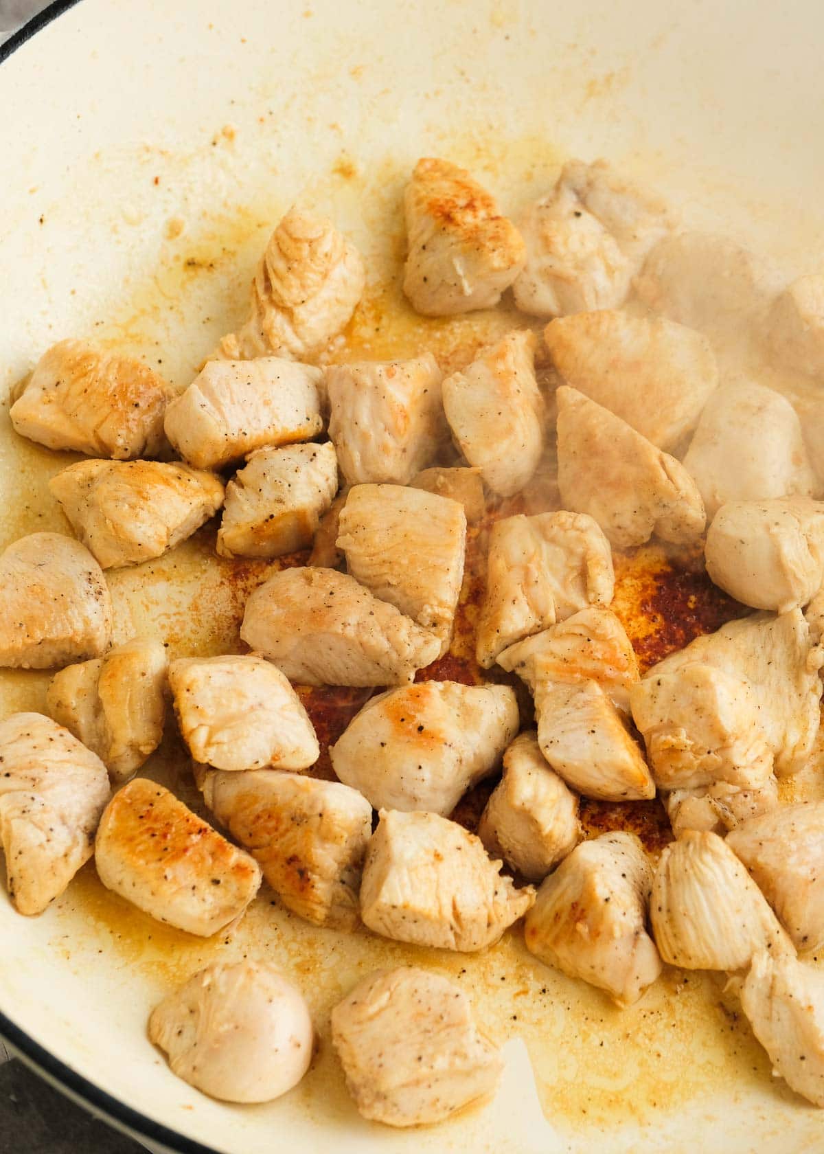 cubed chicken browning in a large skillet with olive oil and sesame oil