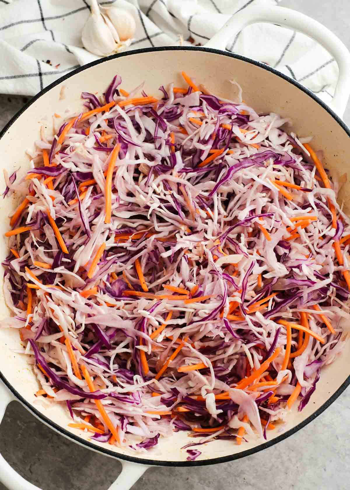 shredded green and purple cabbages with shredded carrots in a skillet