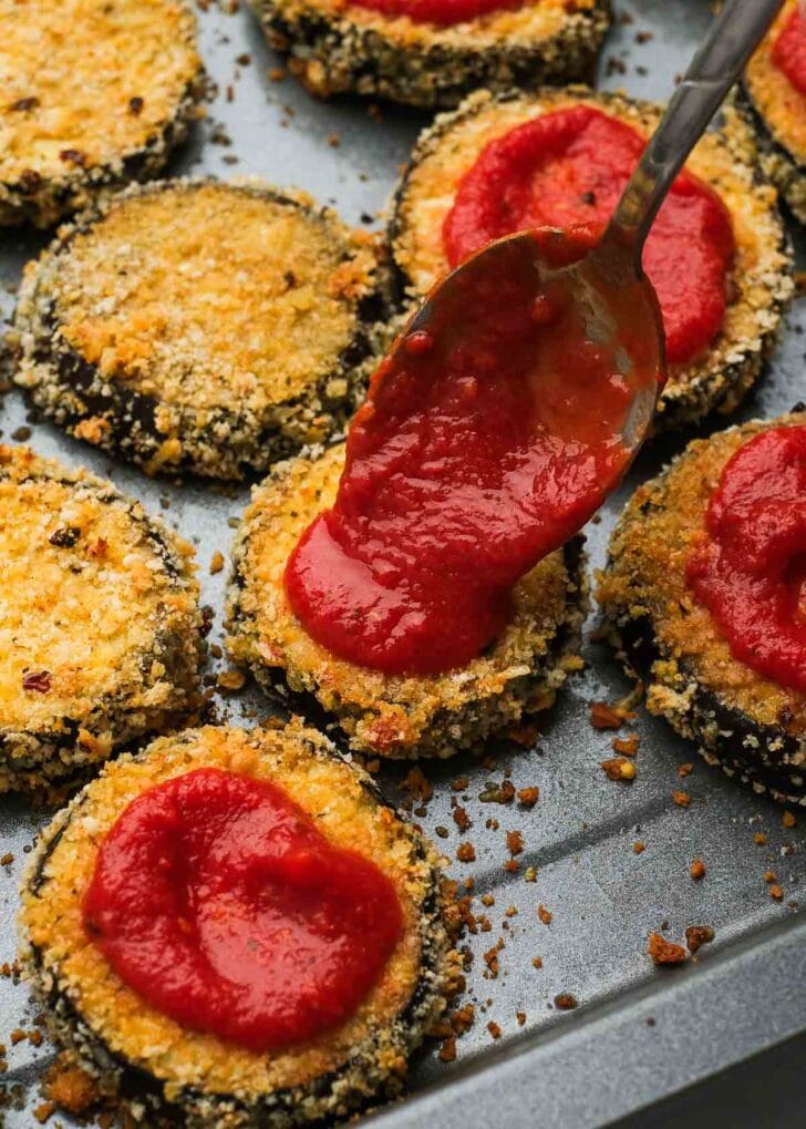 dollops of marinara being spooned onto crispy eggplant bites