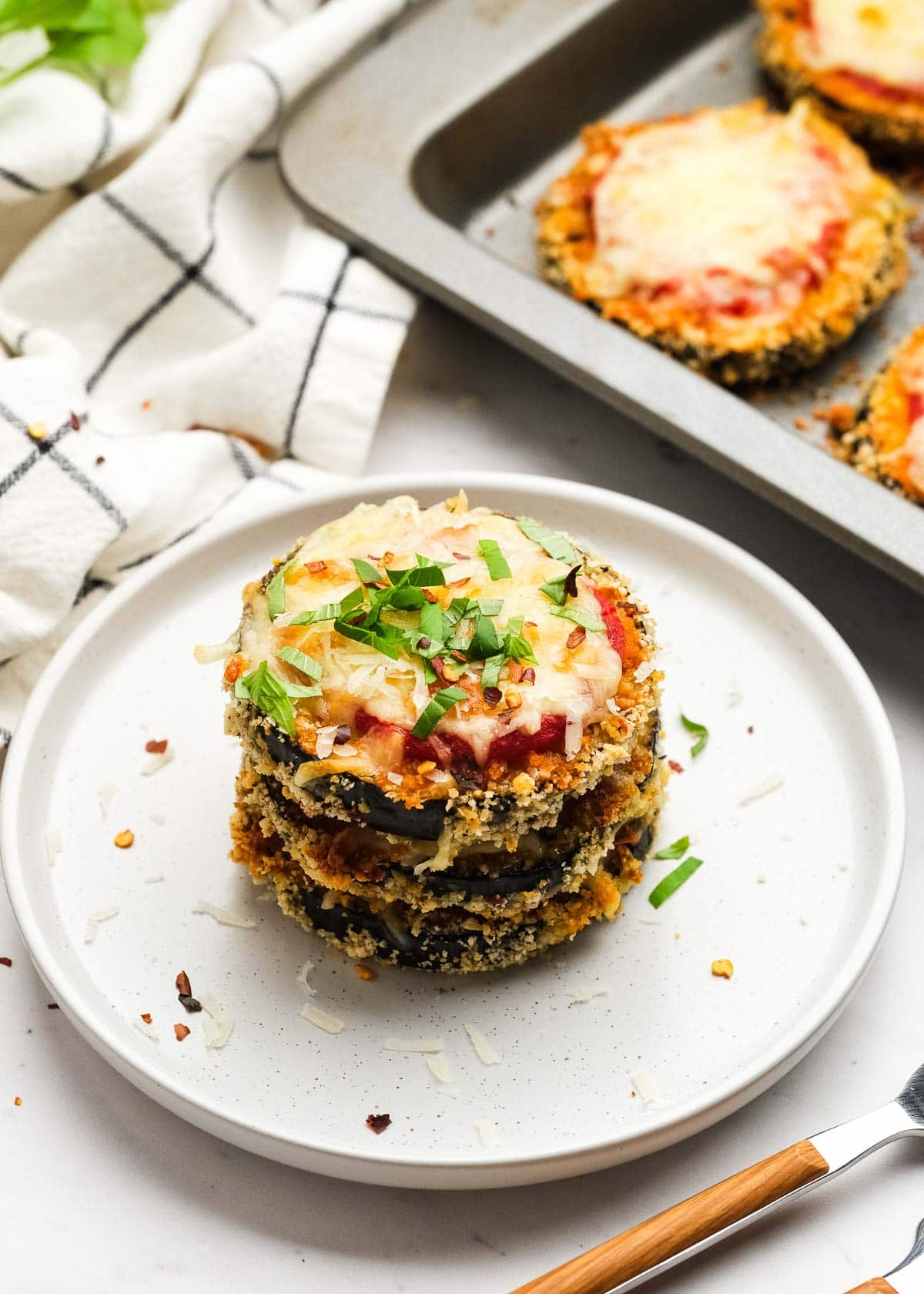 a white plate with 3 breaded eggplant bites in a stack with marinara and mozzarella, garnished with fresh herbs