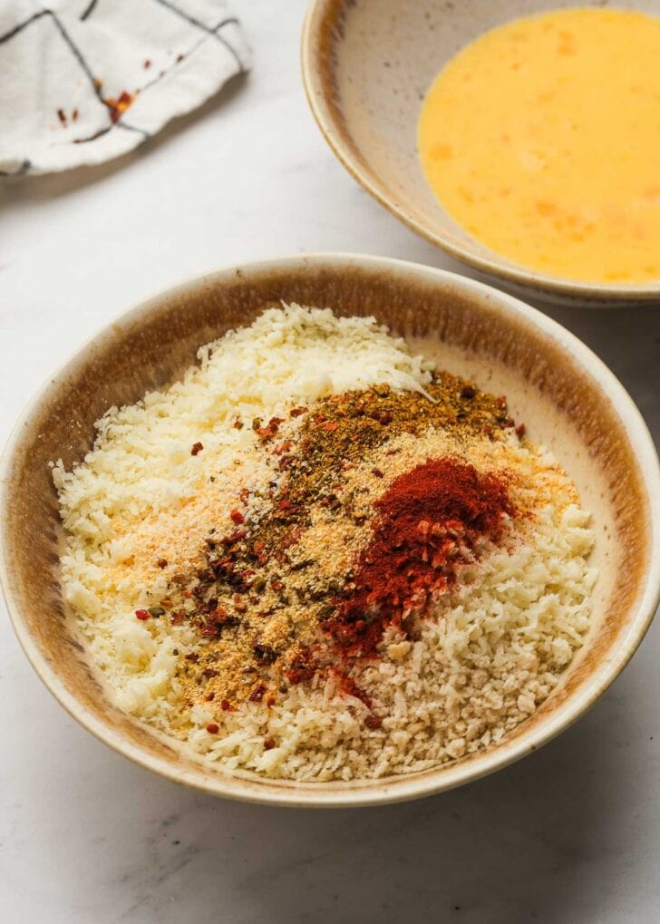 parmesan, panko breadcrumbs, and seasonings in a shallow bowl beside a bowl full of beaten eggs.