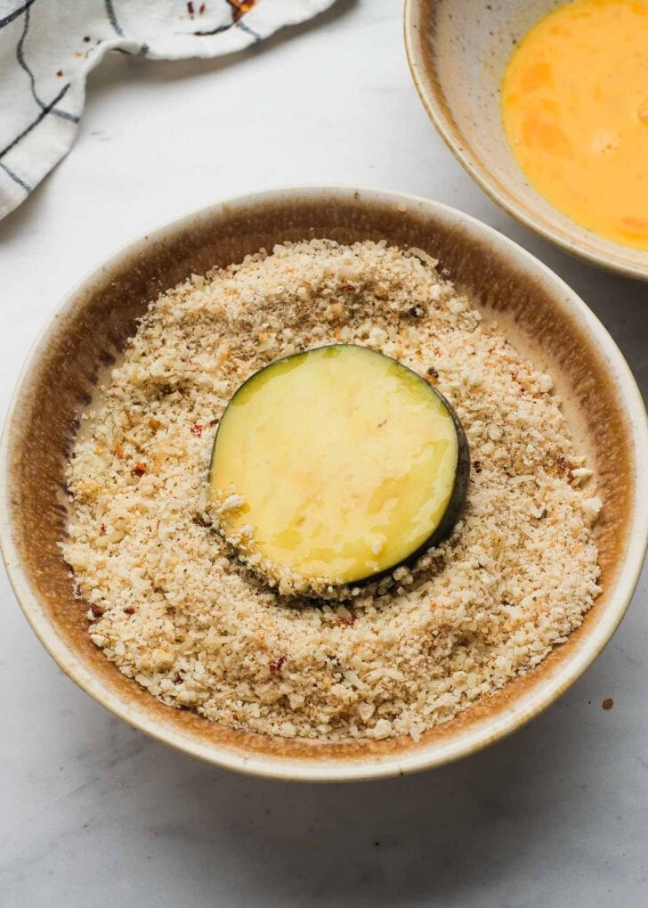 eggplant slice in a bowl of breadcrumbs, parmesan, and seasonings