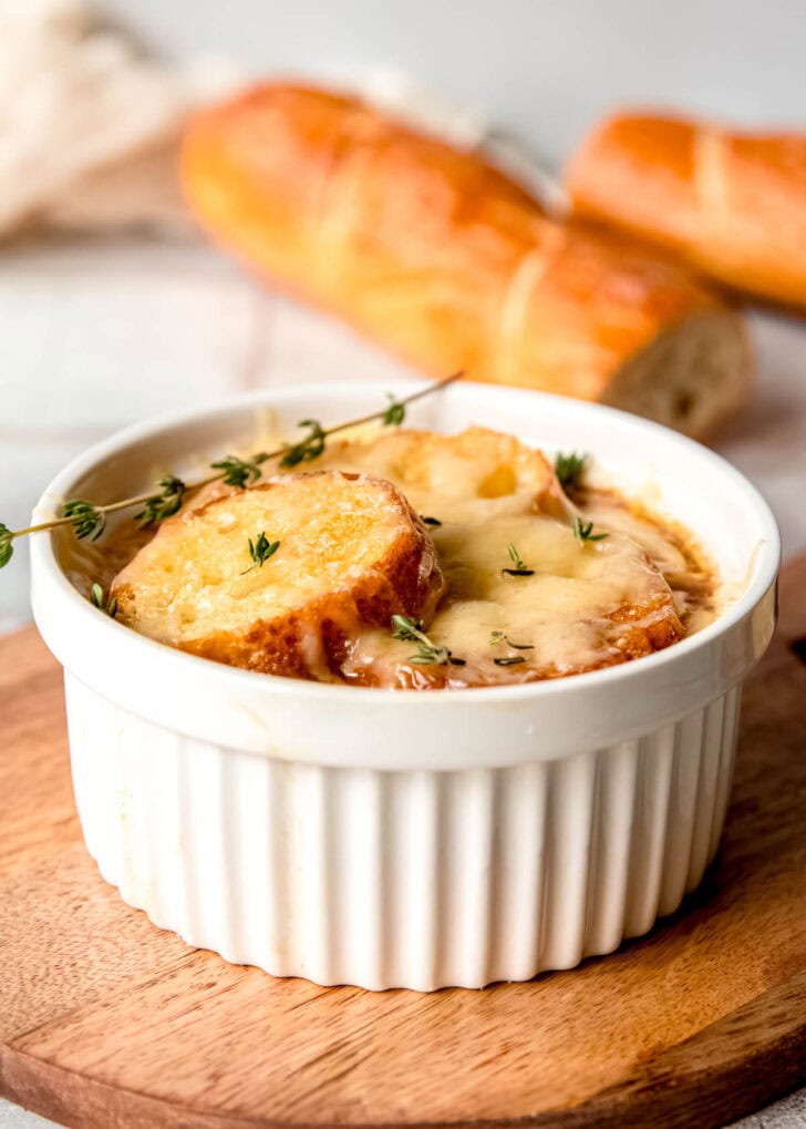 a ramekin full of french onion chicken soup on a cutting board in front of half a baguette