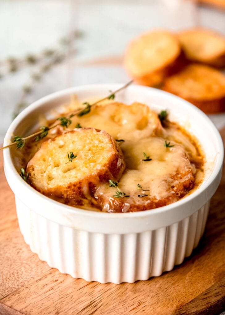 a ramekin full of french onion chicken soup on a cutting board; additional toasted baguette behind.