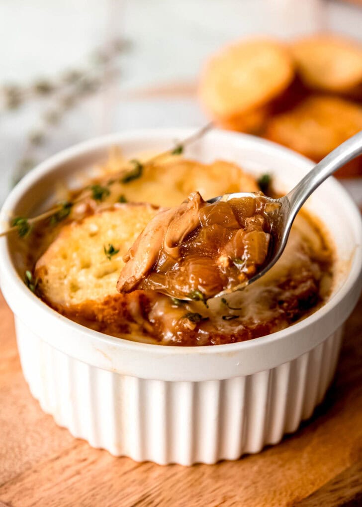 A spoonful of French Onion Chicken Soup over a ramekin full of toasted baguette, melty gruyere, and creamy soup.