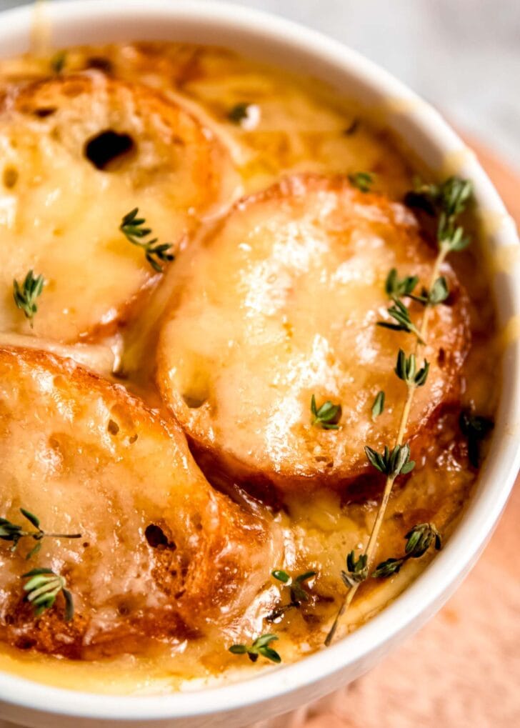 closeup view of golden brown cheese over toasted baguette on a bowl of french onion chicken soup