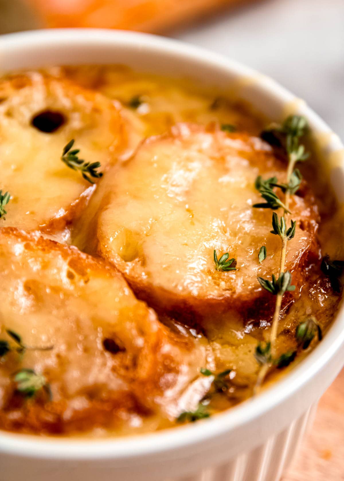 closeup angled view of delicious french onion soup with chicken, toasted baguette slices, and melted gruyere cheese, topped with fresh thyme sprigs