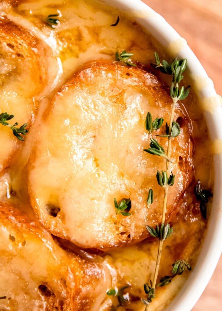 a sprig of fresh thyme garnishing a bowl of french onion chicken soup with toasted bread and melted cheese