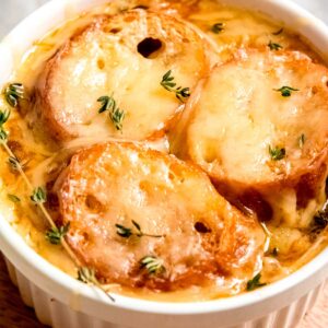 overhead closeup view of white ramekin filled to the brim with french onion chicken soup, toasted baguettes, and melted gruyere cheese