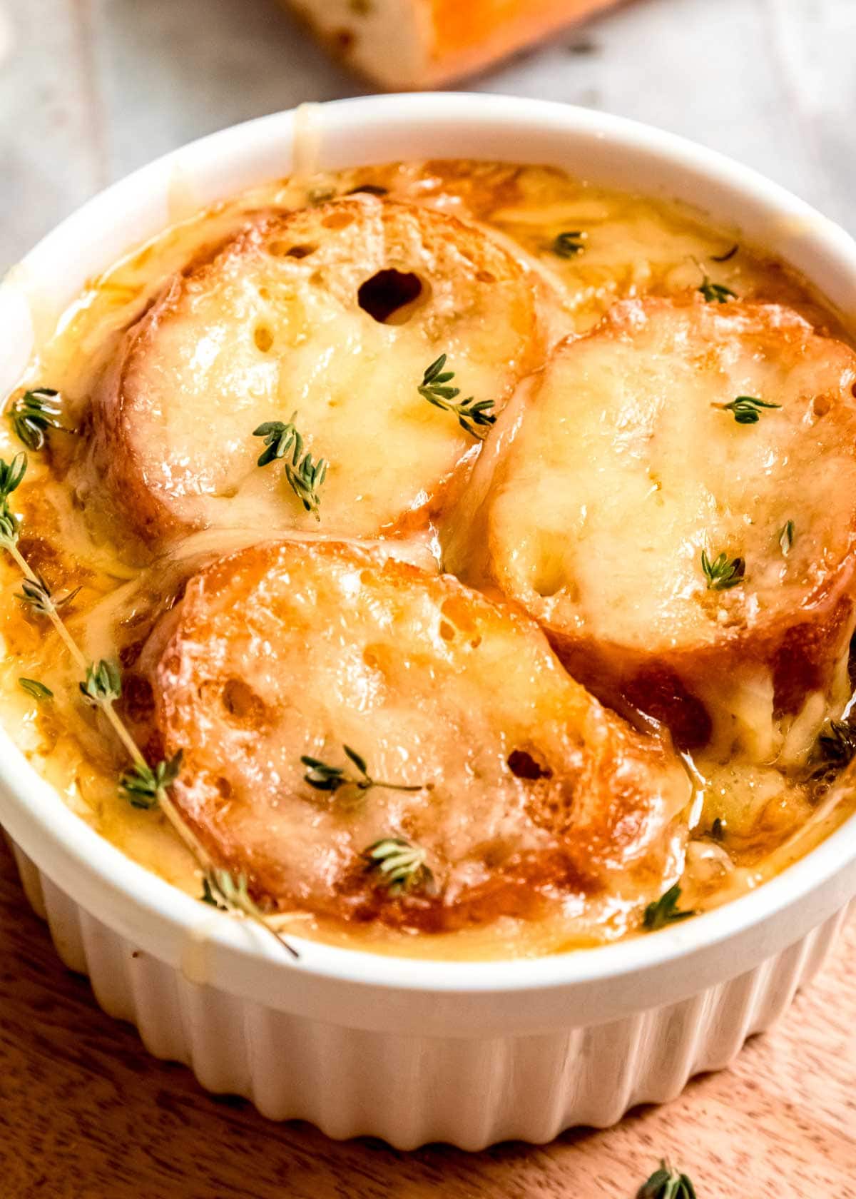 overhead closeup view of white ramekin filled to the brim with french onion chicken soup, toasted baguettes, and melted gruyere cheese