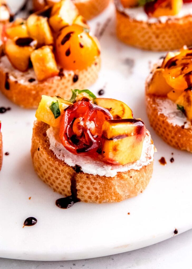 easy peach and tomato bruschetta on a white platter; balsamic reduction drizzled over