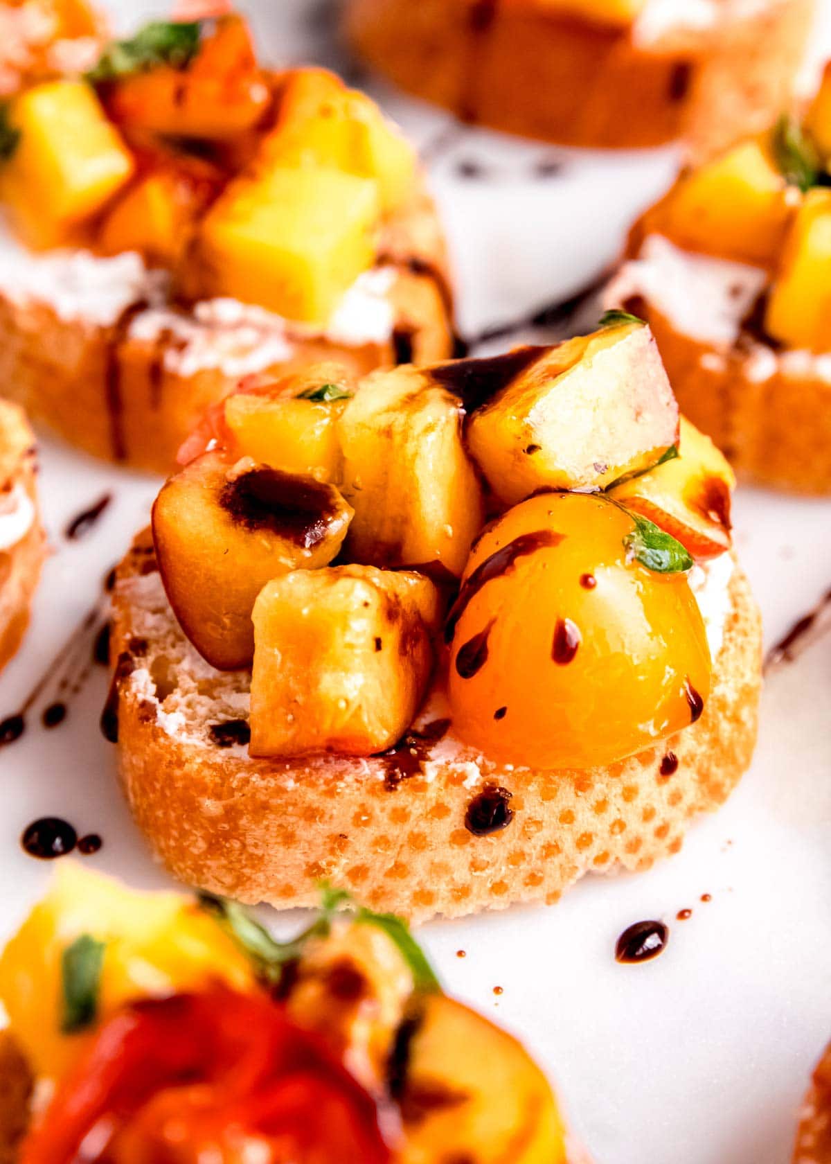 toasted bruschetta covered in creamy goat cheese, peaches, tomatoes, basil, and balsamic reduction for a tasty summer appetizer