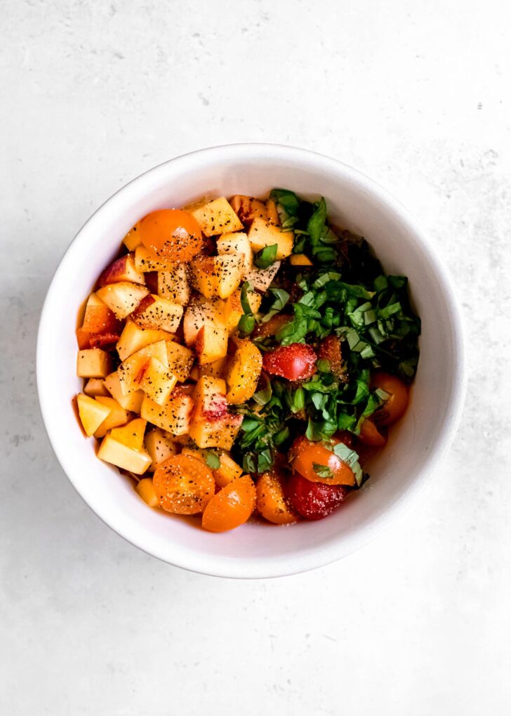 basil, tomatoes, peaches, salt, and pepper in a white bowl