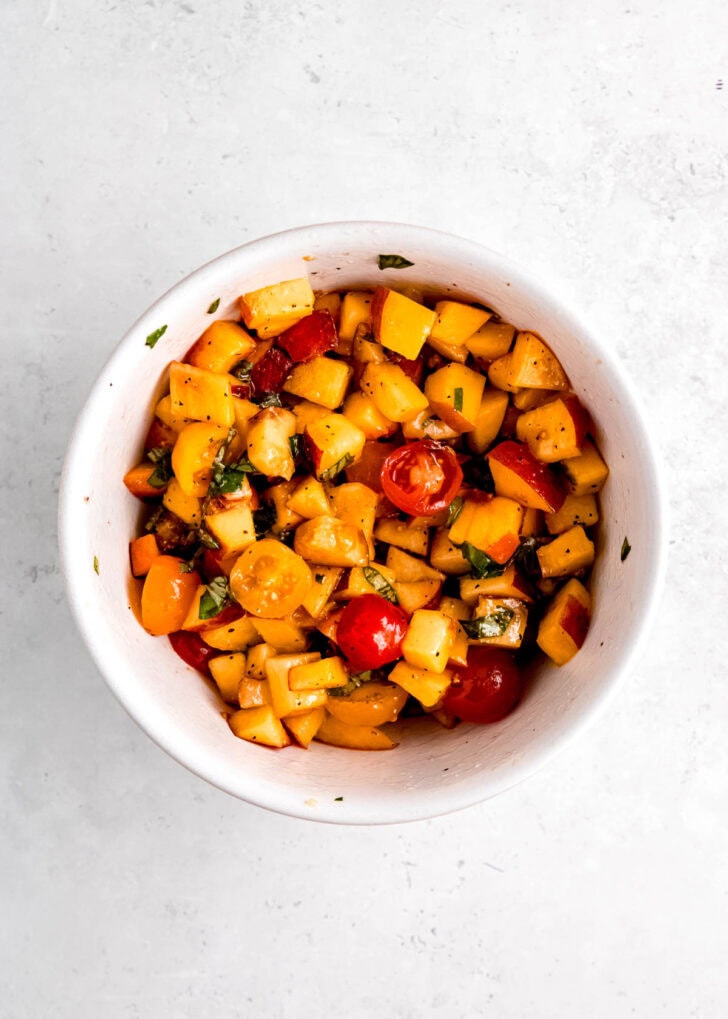 peach and tomato mixture with basil and seasonings in a white bowl