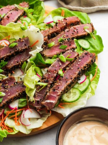 closeup showing rich ahi tuna lettuce wraps with cucumbers, radishes, and carrots in lettuce cups with a creamy dipping sauce on the side