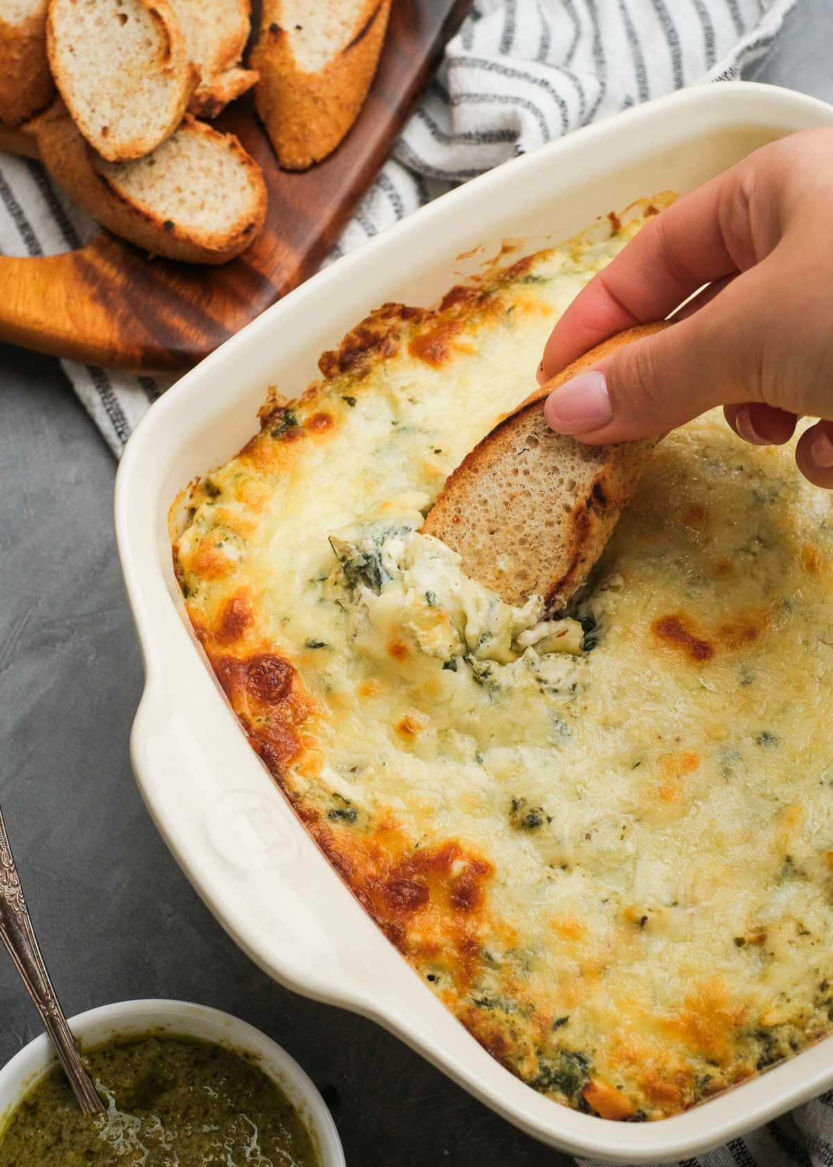 overhead shot of hand dipping bread into creamy pesto chicken dip