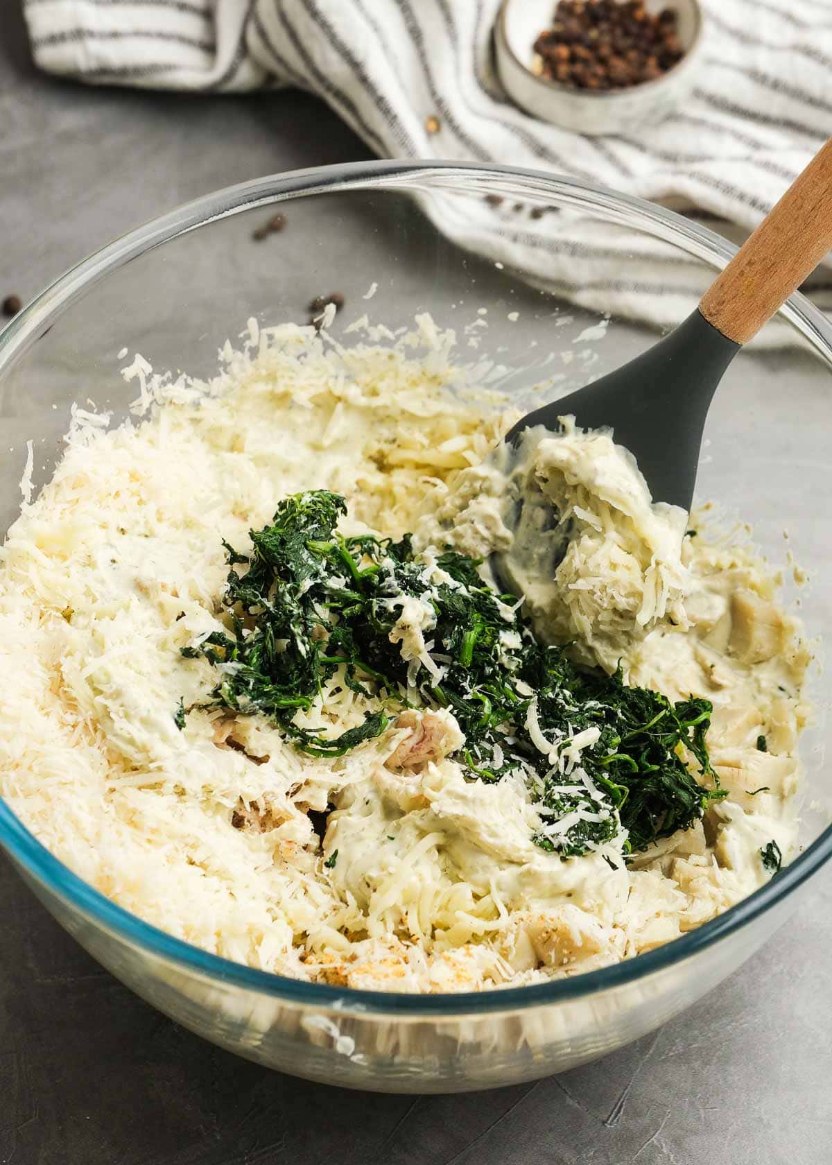 a spatula folding in mozzarella, parmesan, spinach, artichokes, and chicken