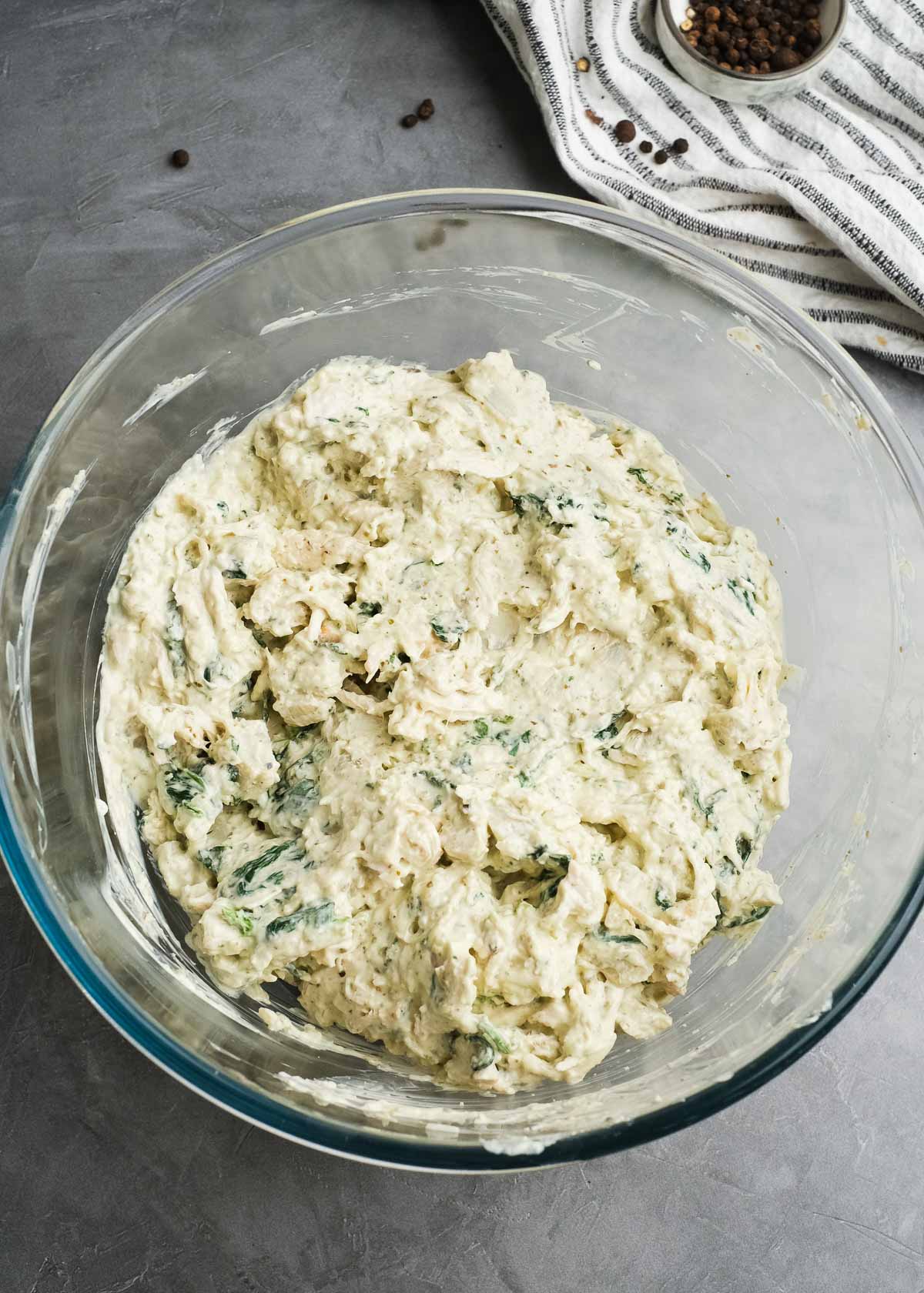 a glass bowl with creamy pesto chicken dip ingredients mixed together