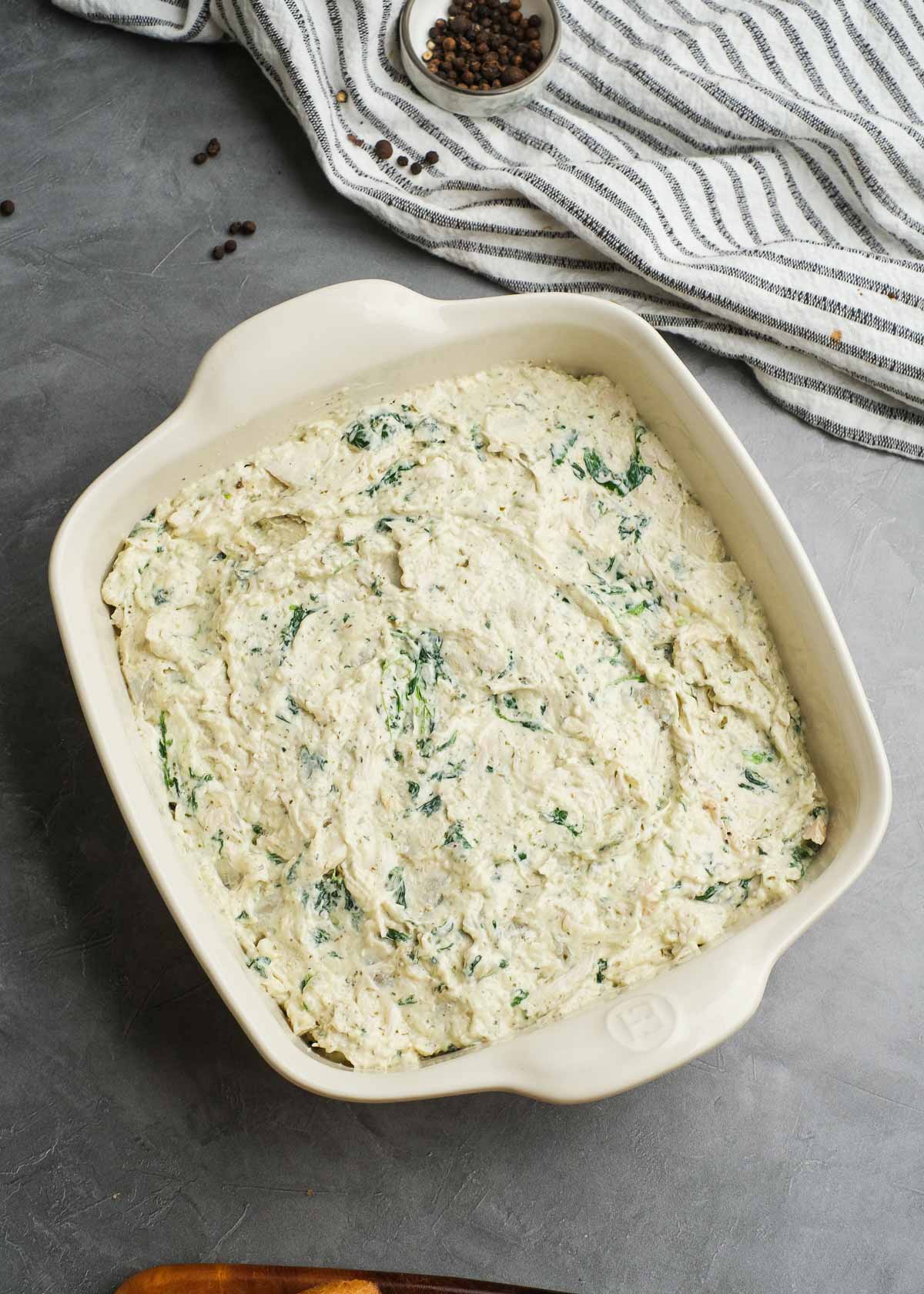 creamy pesto chicken dip spread evenly in a baking dish