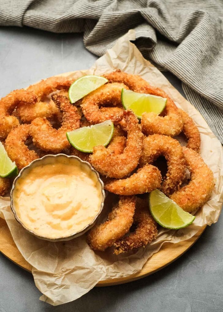 overhead shot showing a wooden board lined with parchment paper and topped with a pile of popcorn shrimp, citrus wedges, and a ramekin of creamy dipping sauce