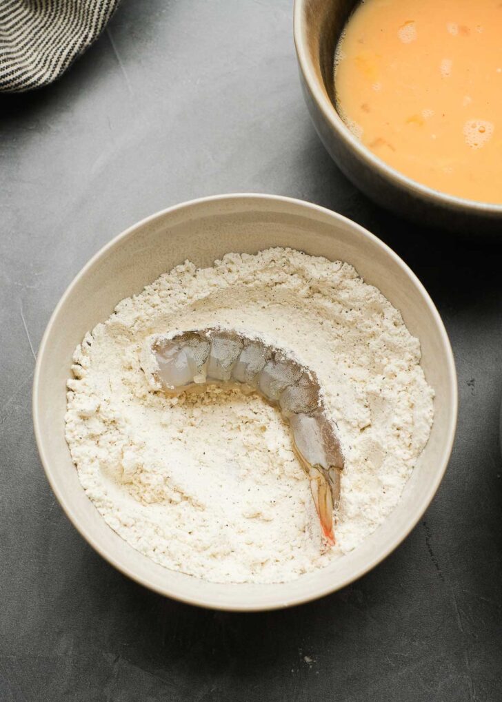 a large tail-on shrimp in a bowl with gluten-free flour, salt, and pepper