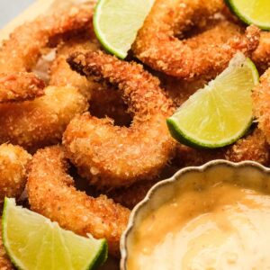 closeup showing crunchy popcorn shrimp with lime wedges and a side of dipping sauce