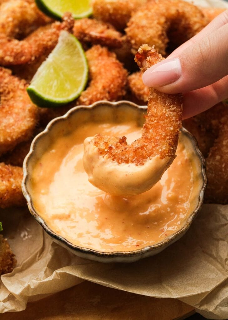 a hand dipping a piece of popcorn shrimp in the creamy, flavorful sauce