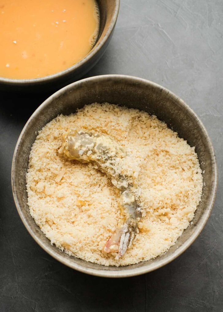 a large shrimp coated in flour and egg mixtures, now rolling in a seasoned breadcrumb mixture