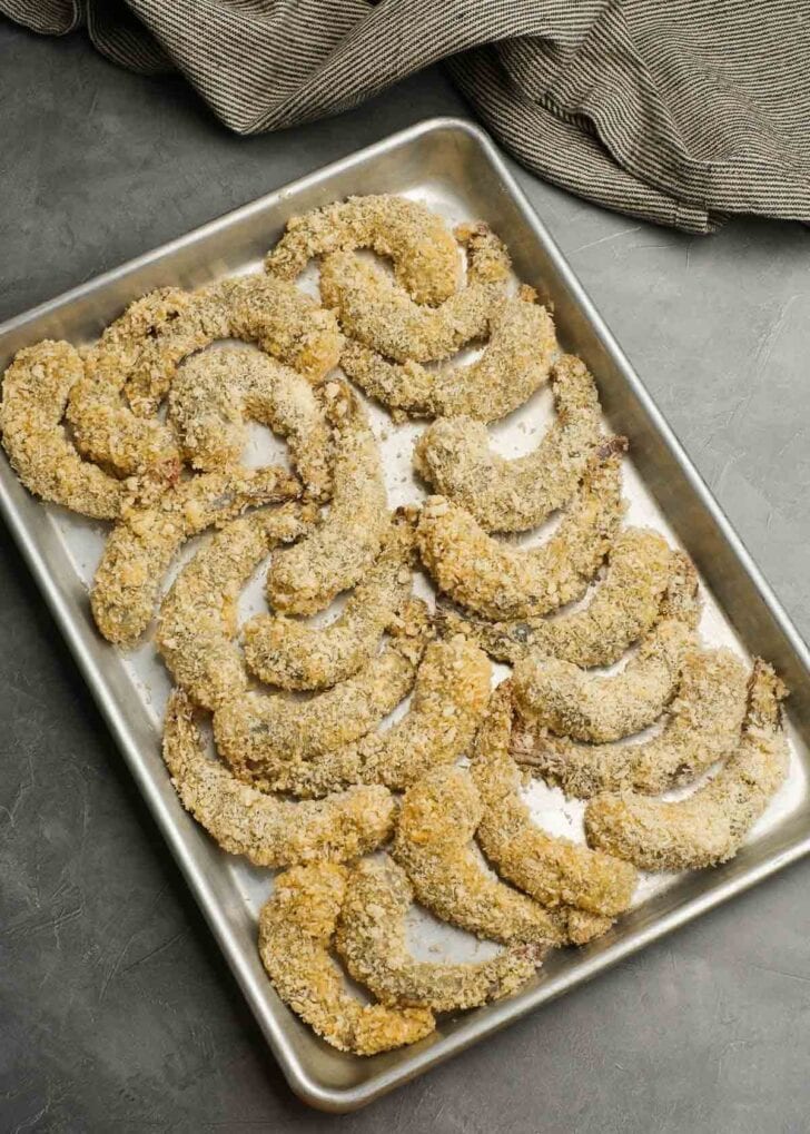 a baking sheet full of breaded shrimp ready to be fried