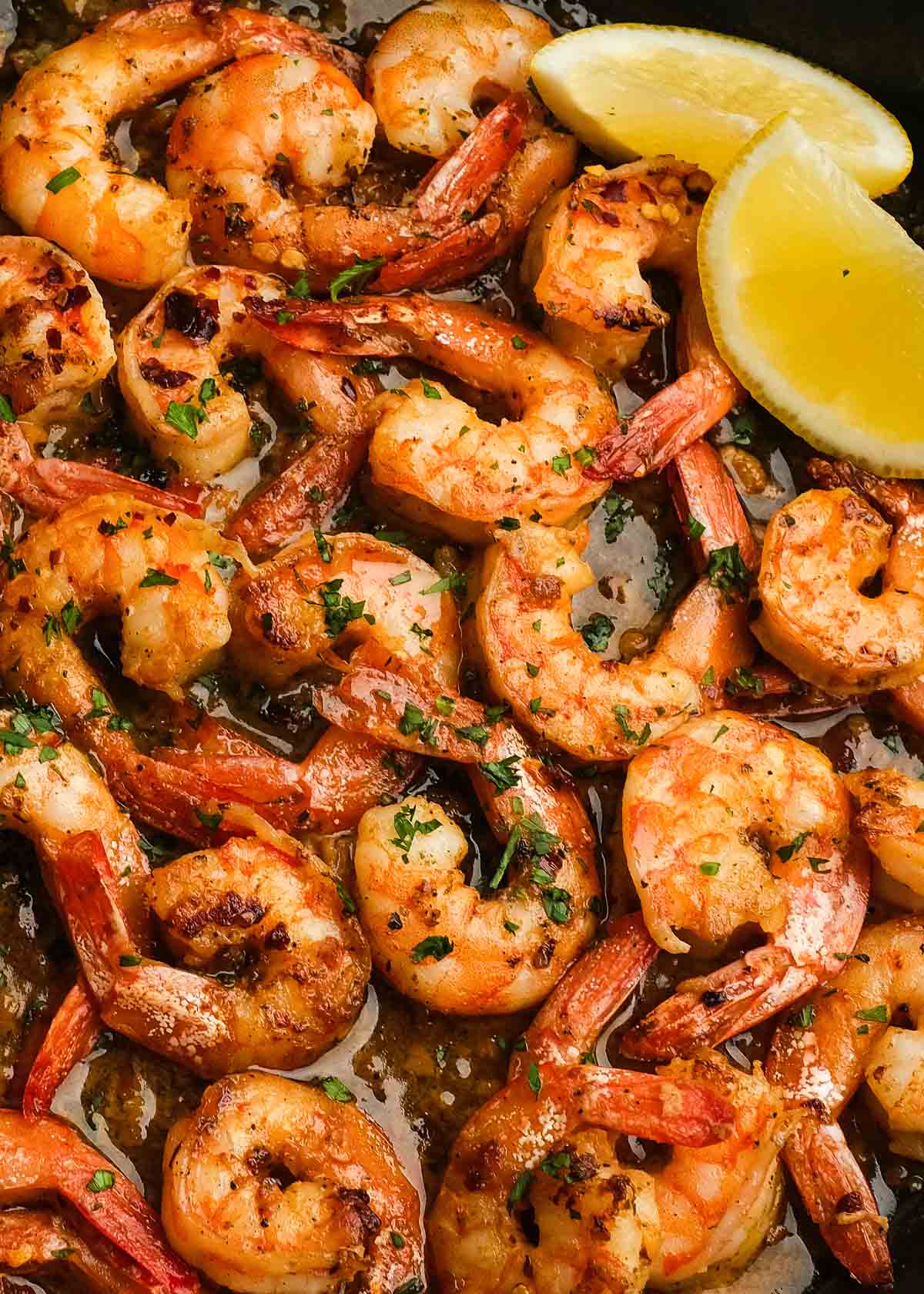 juicy shrimp covered in garlic butter sauce in a pan, garnished with fresh herbs and lemon wedges on the side