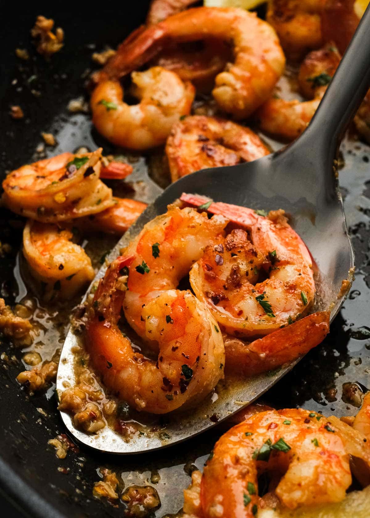 a spoon of juicy shrimp scampi in a black skillet filled with succulent shrimp covered in garlic butter white wine sauce