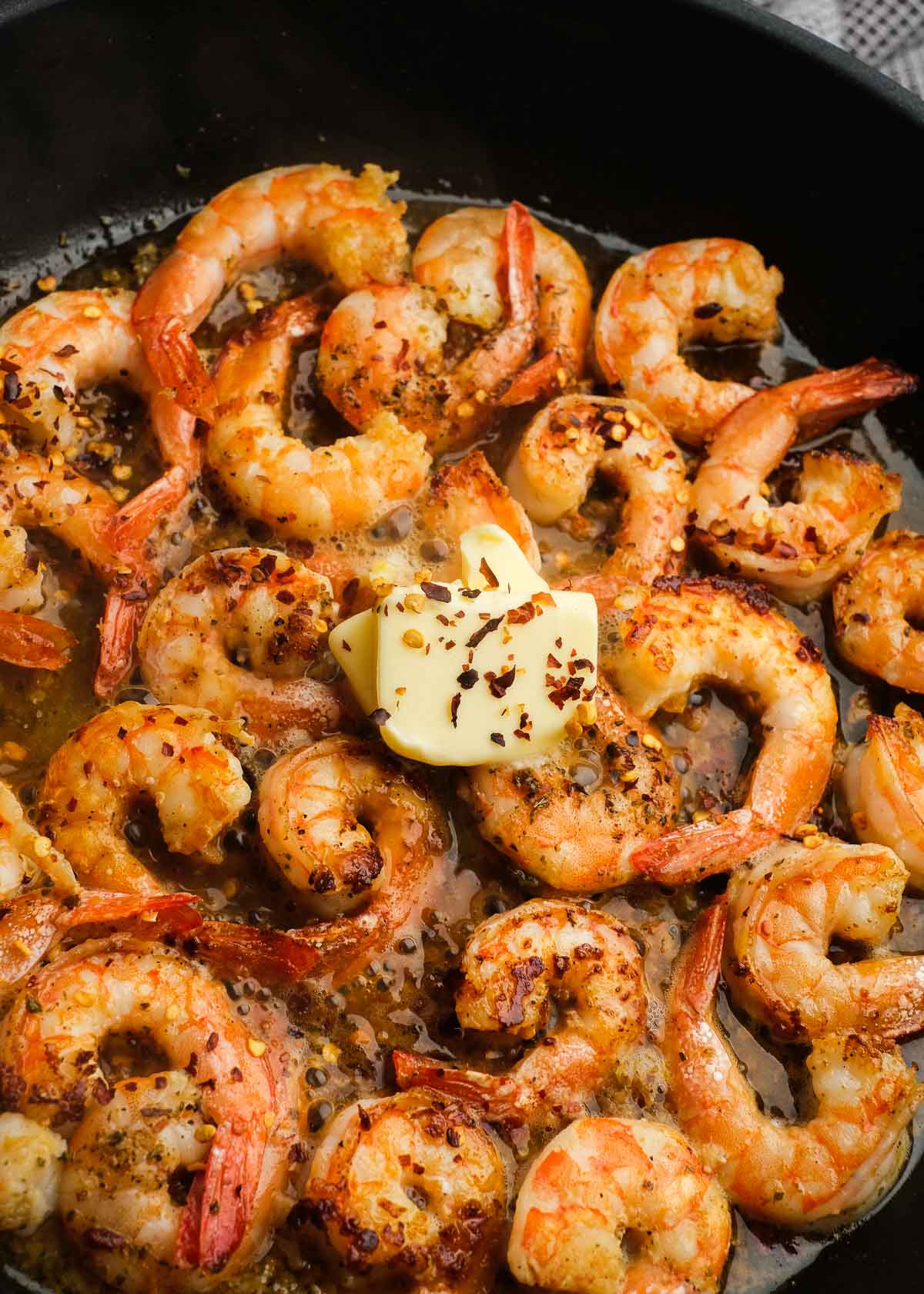 butter and red pepper flakes added to shrimp scampi cooking in a black skillet